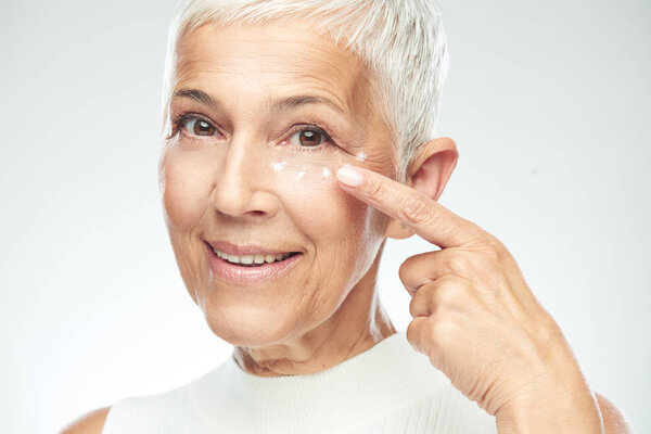 Gorgeous smiling Caucasian senior woman trying out new anti age cream. Beauty photography.