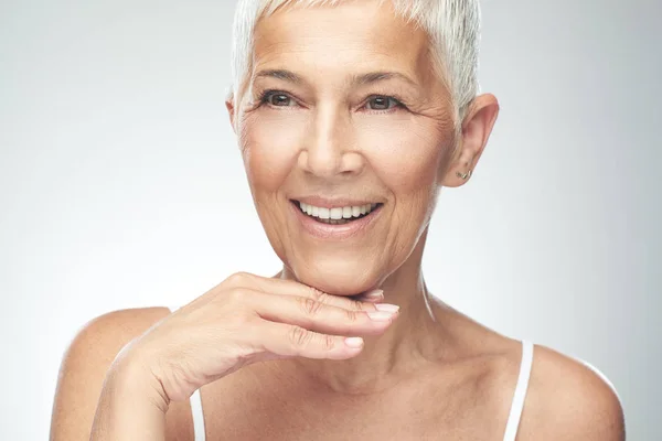 Beautiful smiling senior woman with short gray hair posing in front of gray background. Beauty photography. Royalty Free Stock Images