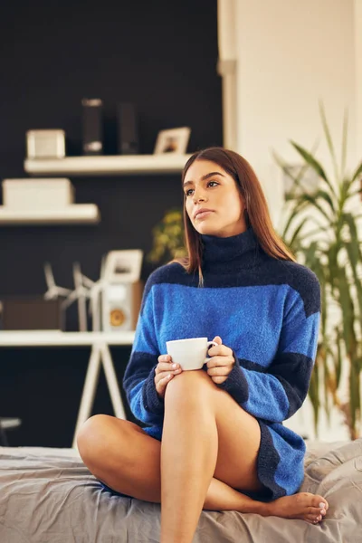 Charmante Brünette in blauem Pullover sitzt morgens im Schlafzimmer und trinkt Kaffee. — Stockfoto