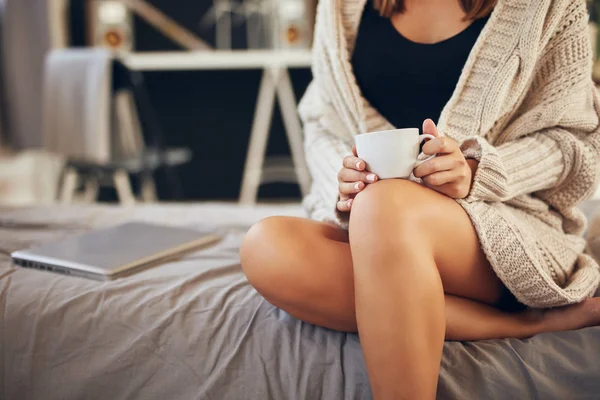 Abgeschnittenes Bild einer kaukasischen Frau im Pullover, die eine Tasse Kaffee hält, während sie im Schlafzimmer auf dem Bett sitzt. — Stockfoto