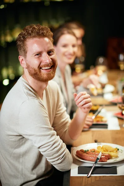 Guapo caucásico barbudo jengibre sentado en el restaurante con sus amigos y cenar . — Foto de Stock