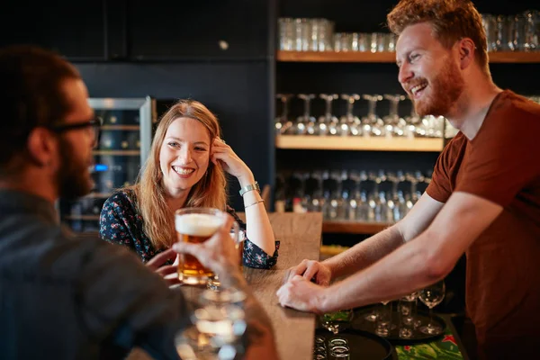 Fröhliche Freunde lehnen an der Theke, trinken Bier und unterhalten sich mit dem Barkeeper. Ausgehen. — Stockfoto