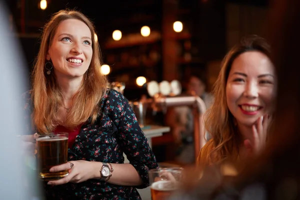 Zwei schöne kaukasische Mädchen, die Bier in der Hand halten, plaudern und sich in der Kneipe amüsieren. Ausgehen. — Stockfoto