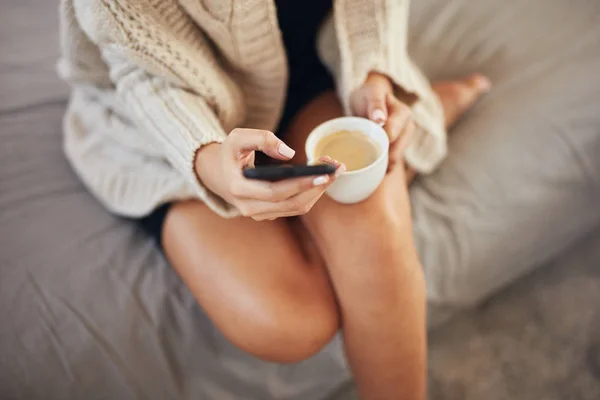 Вид сверху на женщину, которая пользуется смартфоном и держит чашку кофе, сидя утром в постели . — стоковое фото