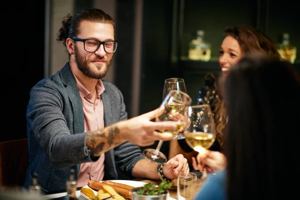 Beste vrienden zitten in restaurant voor het diner en het maken van een toast met witte wijn. Op tafel is eten. — Stockfoto