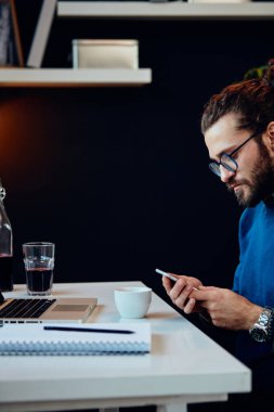 Ofisinde oturan ve akıllı telefon kullanan hippilerin yan görüntüsü..