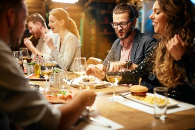 Bir grup neşeli arkadaş restoranda oturmuş, sohbet ediyor ve yemek yiyorlar..