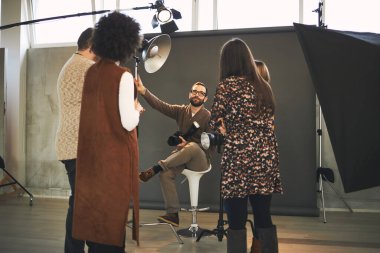 Genç yakışıklı sakallı eğitimci, çok kültürlü katılımcılarına kameranın nasıl çalıştığını gösteriyor. Fotoğraf stüdyosunun içi.