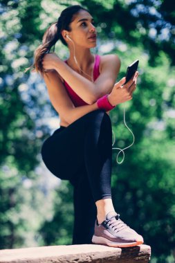 Genç ve çekici beyaz kadın koşuya ara veriyor ve akıllı telefon kullanıyor..