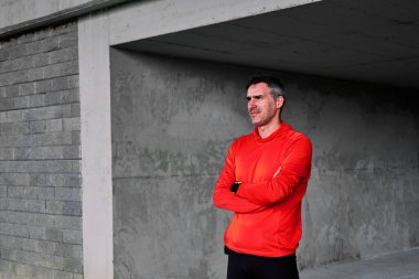 Orta yaşlı gururlu koşucu kollarını kavuşturarak dışarıda duruyor..