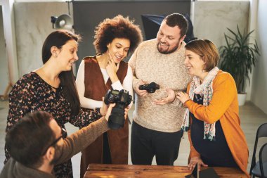 Genç yakışıklı sakallı eğitimci, çok kültürlü katılımcılarına kameranın nasıl çalıştığını gösteriyor. Fotoğraf stüdyosunun içi.