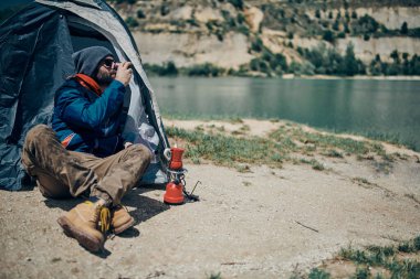 Yakışıklı sakallı adam çadırda oturuyor, dinleniyor ve doğada kahve içiyor..