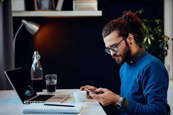 Sidovy Allvarliga Hipster Sitter Sitt Kontor Och Använder Smarttelefon — Stockfoto