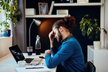 Genç sakallı hippi evinde oturuyor ve başı ağrıyor çünkü çok çalışıyor..