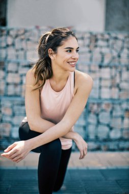 Genç gülümseyen pozitif bayan koşucu bacaklarını esnetiyor ve şehir dışında koşmaya hazırlanıyor..