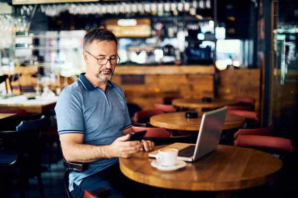 Volwassen Man Zit Koffieshop Gebruikt Een Smartphone Staat Een Koffie — Stockfoto