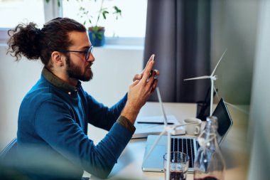 Genç çekici hippi evinde oturuyor ve Corona virüsü sırasında akıllı telefon kullanıyor..