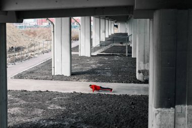 Eşofmanlı ve kırmızı kazaklı çekici genç sporcu şehir dışında şınav çekiyor..