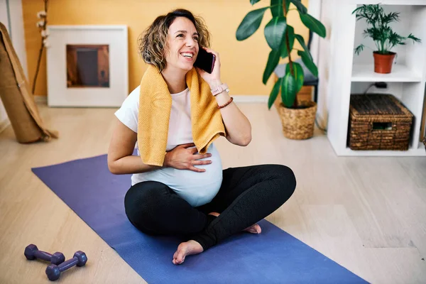 家の床の上に座って休憩を取り電話で話している幸せな中年の妊娠中のスポーツ女性を笑顔 — ストック写真