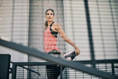 Sporcu kadın şehir dışında koşmadan önce bacağını esnetiyor..