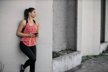 Sporcu kadın duvara yaslanıyor ve telefona bir mesaj yazıyor..