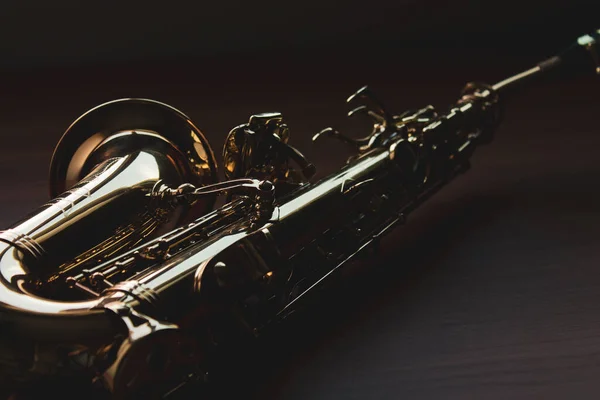 Dark closeup of saxophone on a wood surface.