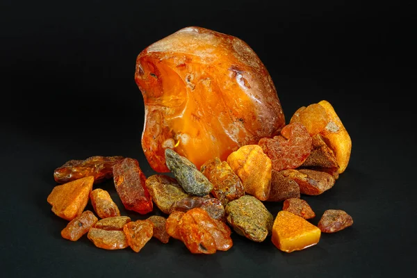 Amber. Composition of several pieces of amber of different colors and shapes on a black background, Petrified fossil resin. Copal. Sun stone. Natural mineral. Material for jewelers. Unprocessed pieces of amber with a crust. Yellow resin