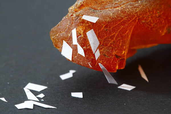 Физические свойства янтаря. Электростатика. Кусок янтаря притягивает к себе кусочки бумаги. Большой полупрозрачный кусок желтого янтаря, намагниченный электричеством на черном фоне. Ископаемая ископаемая смола. Солнечный камень. Электромагнетизм