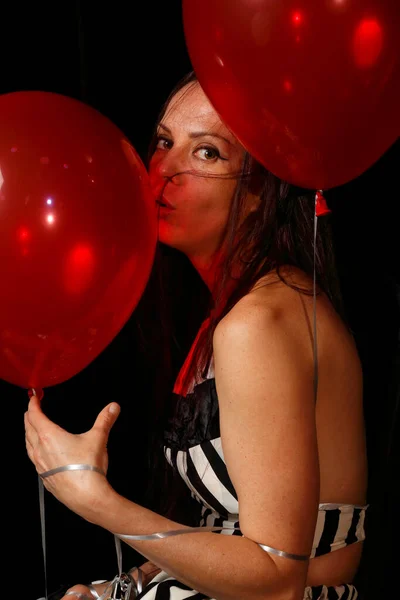 Girl with red balloons on a dark background. Brunette model in striped clothes on black. Place for text. Portrait of a beautiful woman. Gaze. Photo session in the studio. Fashion and beauty. Art. Room decoration poster. Luxury