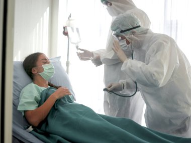 Corona virüsü için hastalık tedavi odası hastaya bulaştı. Hasta, hastanede karantinada koruyucu giysiler giyen doktorla yatakta yatıyor.