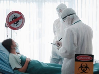 Corona virüsü için hastalık tedavi odası hastayı karantina ve salgın uyarısı ile enfekte etti. Hasta, hastanede karantinada koruyucu giysiler giyen bir doktorla yatakta yatıyor.