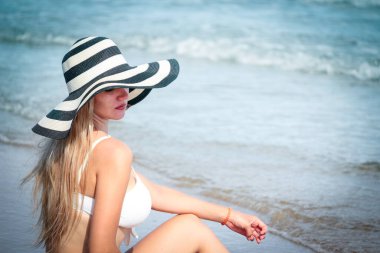 Mutlu yaz tatili, beyaz bikinili ve şapkalı seksi sarışın kadınlar plajda eğleniyor, dinleniyor ve mavi denizli tropikal adada dinleniyor.