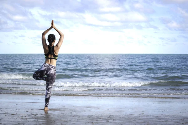 Genç güzel atlet kadın yoga yapıyor ve vücudunu esnetiyor. Yaz mevsiminde tropikal ada sahillerinde mavi denizde, spor yapan kadın dışarıda egzersiz yapıyor ve antrenman yapıyor.