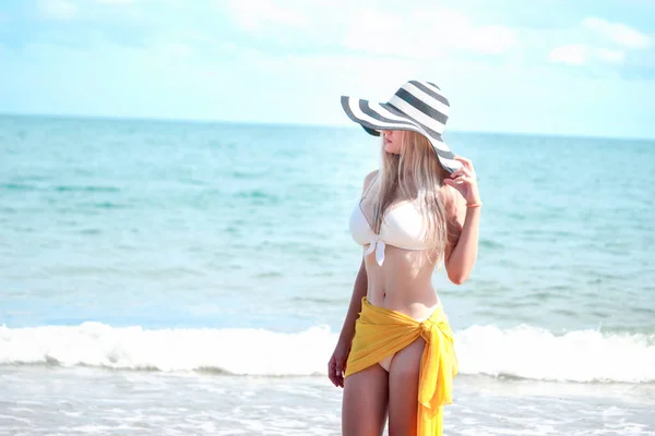 幸せな夏休み 白いビキニの熱いセクシーな美しいブロンドの女性とビーチで楽しんでいる黄色のショールで帽子 休息と青い海と熱帯の島でリラックスする時間を過ごす — ストック写真