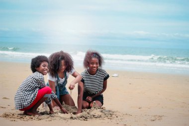 Tatlı çocuklar kumlu yaz kumsalında mavi denizle birlikte eğleniyorlar, mutlu çocukluk arkadaşı kumdan kale yapıyor, tropik plajda kumla oynuyor.