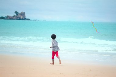 Tatlı çocuk kumlu yaz kumsalında mavi denizle eğleniyor. Mutlu çocukluk çocuğu tropik plajda renkli uçurtma oynuyor.
