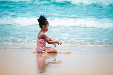 Şirin bir çocuk kumlu sahilde mavi denizle eğleniyor. Tropikal sahilde oynayan mutlu küçük bir kız.