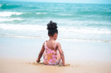 Şirin bir çocuk kumlu sahilde mavi denizle eğleniyor. Tropikal sahilde oynayan mutlu küçük bir kız.