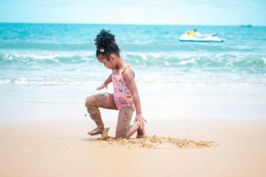 Şirin bir çocuk kumlu sahilde mavi denizle eğleniyor. Tropikal sahilde oynayan mutlu küçük bir kız.