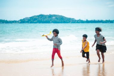 Tatlı çocuklar kumlu yaz kumsalında mavi denizle eğleniyor, mutlu bir çocukluk çocuğu ve kız tropik plajda model uçak oynuyor ve koşuyor.