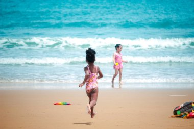 Küçük şirin kız kumlu bir yaz günü mavi denizle eğleniyor. Mutlu çocukluk arkadaşı tropikal plajda koşuyor ve oynuyor. 