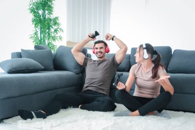 Genç çift evde video oyunu oynuyor, erkek kaldırma oyunu kazanıyor, kaybeden kadın üzülüyor, insanlar oturma odasında oturup oyun konsolu kullanıyor, gençler evde dinleniyor.