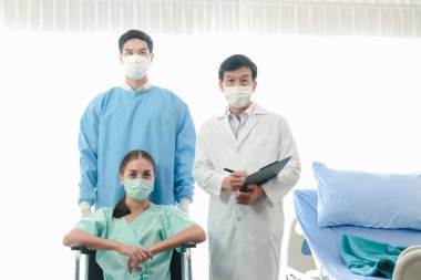 Kadın hasta tekerlekli sandalyede maske takıyor. Arkasında iki doktor var. Sağlık hizmetleri ve hastane konsepti.