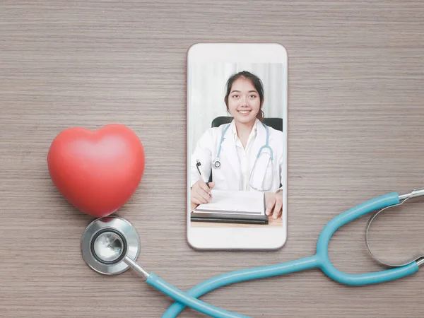 Doctor online concept, red heart with stethoscope and a doctor on smartphone screen for online consultation with patient, online medical communication on virtual interface, virtual hospital