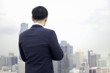 Güvenlik kaskı takmış iş adamının sırtında gökyüzüne gökdelen şehriyle bakıyor ve geleceğe doğru yol alıyor.
