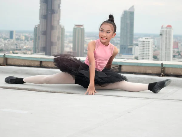 Asian ballerina dancer girl practicing ballet dancing on rooftop with skyscraper city view, adorable child dancing in ballet