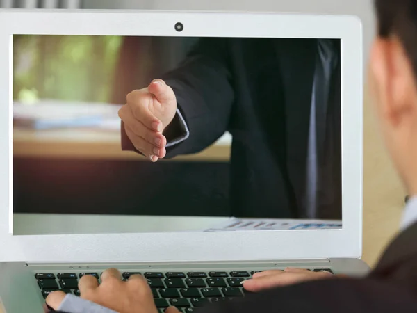 Back view of businessman meeting online in video conference, communicates on video call with work colleagues using a laptop, businessman on computer screen giving hand for handshake to seal a deal