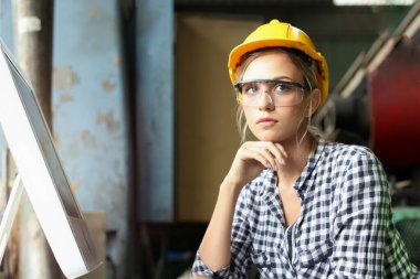 Kask takan, güvenlik gözlüğü takan, bilgisayar kullanan, fabrika fabrikasında çalışan genç ve güzel kadın endüstriyel mühendisin portresi.