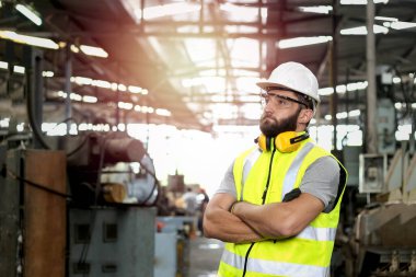 Sanayi mühendisi portresi miğfer ve güvenli gözlük takıyor. Fabrika fabrikasında kolları çapraz duruyor.