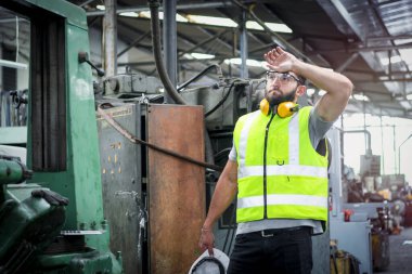 Güvenli gözlük ve güvenlik süiti takmış, miğfer tutan yorgun bir endüstri mühendisi. Fabrika fabrikasında çalışan çalışkan bir adam..